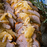 Sliced roasted pork tenderloin topped with caramelized onions and a glossy sauce, garnished with a sprig of fresh rosemary on the side.
