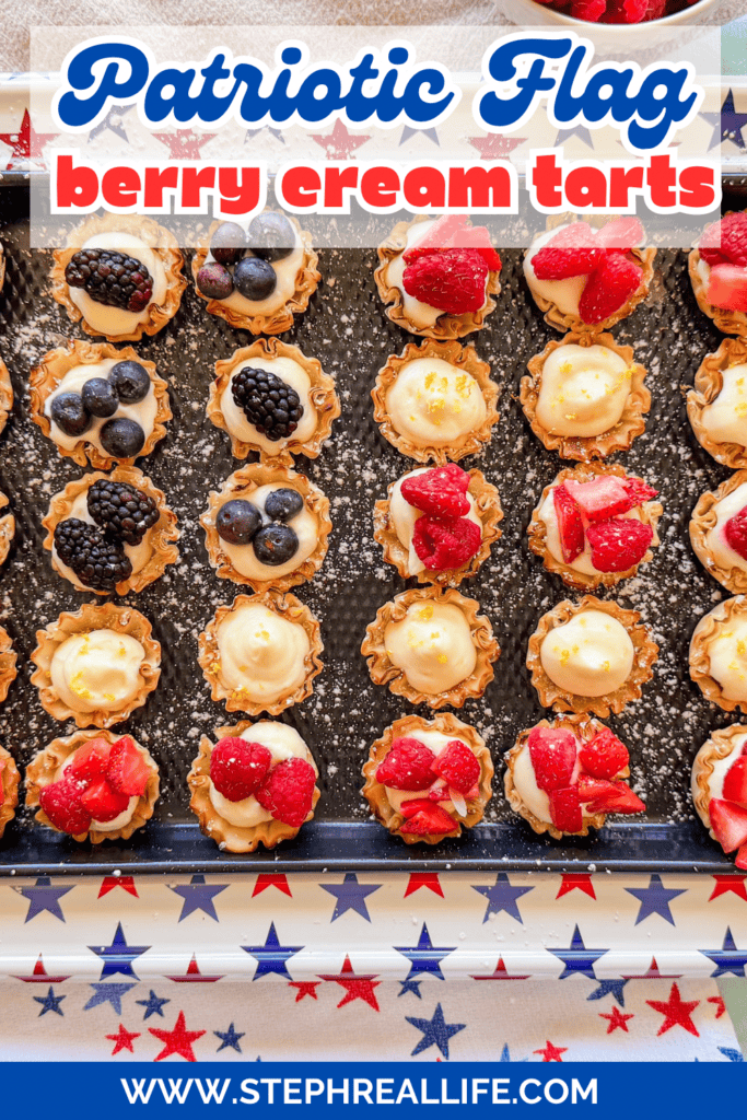A tray of mini berry cream tarts topped with strawberries, blueberries, and blackberries sits on a star-spangled tablecloth, with text reading Patriotic Flag berry cream tarts and a website URL at the bottom.