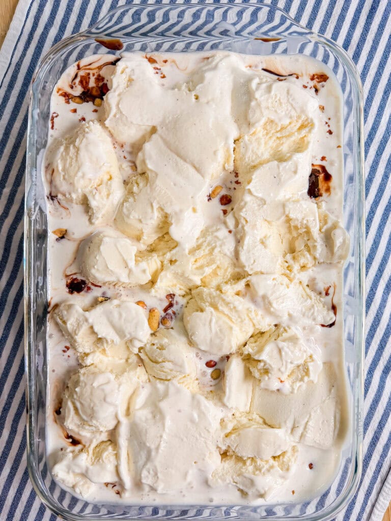 A glass dish filled with creamy vanilla ice cream, swirled with chocolate syrup, sits on a blue and white striped cloth.