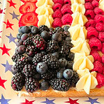 A dessert arranged like the American flag with blackberries and blueberries for the stars section, and rows of strawberries, raspberries, and frosting for the stripes, on a star-patterned tray.