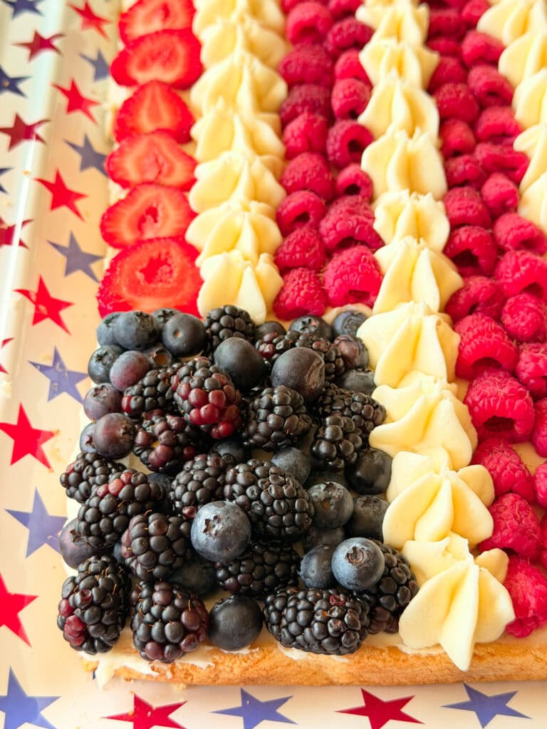 A dessert arranged like the American flag with blackberries and blueberries for the stars section, and rows of strawberries, raspberries, and frosting for the stripes, on a star-patterned tray.
