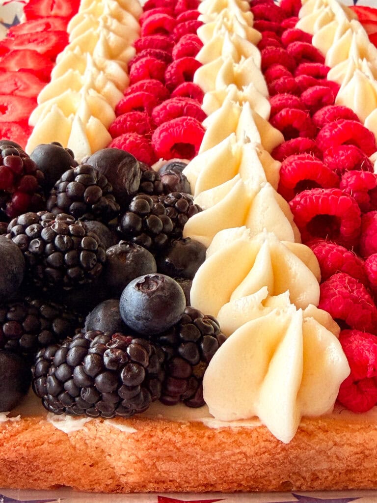 A rectangular cake decorated with rows of fresh blackberries, blueberries, raspberries, and piped white frosting, arranged in a pattern resembling the American flag.