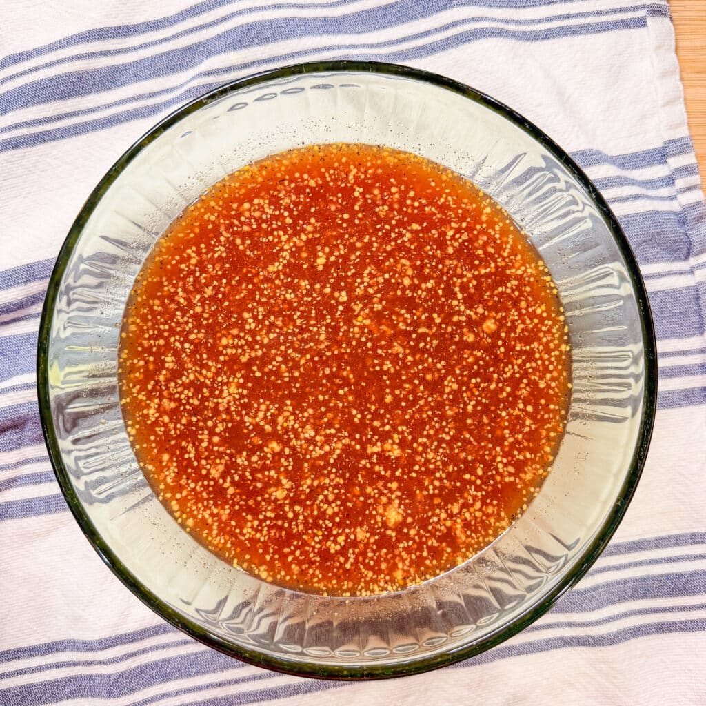 A glass bowl filled with an orange-red liquid containing visible small yellowish granules, placed on a white cloth with blue stripes.