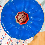 A blue gelatin dessert in a bundt mold sits on a plate. Underneath are two towels with red and blue star patterns, all placed on a wooden surface.