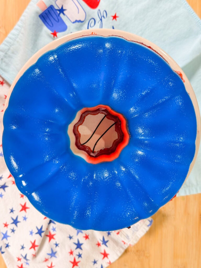 A blue gelatin dessert in a bundt mold sits on a plate. Underneath are two towels with red and blue star patterns, all placed on a wooden surface.
