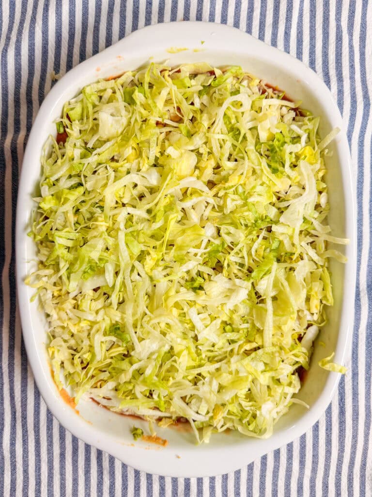 A white oval dish filled with shredded lettuce sits on a blue and white striped cloth.