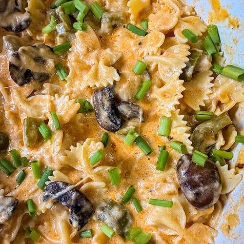 Bowtie pasta in a creamy orange sauce with mushrooms and topped with chopped green onions.