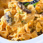 A close-up of creamy bowtie pasta with mushrooms and herbs being lifted from a dish with a spoon.