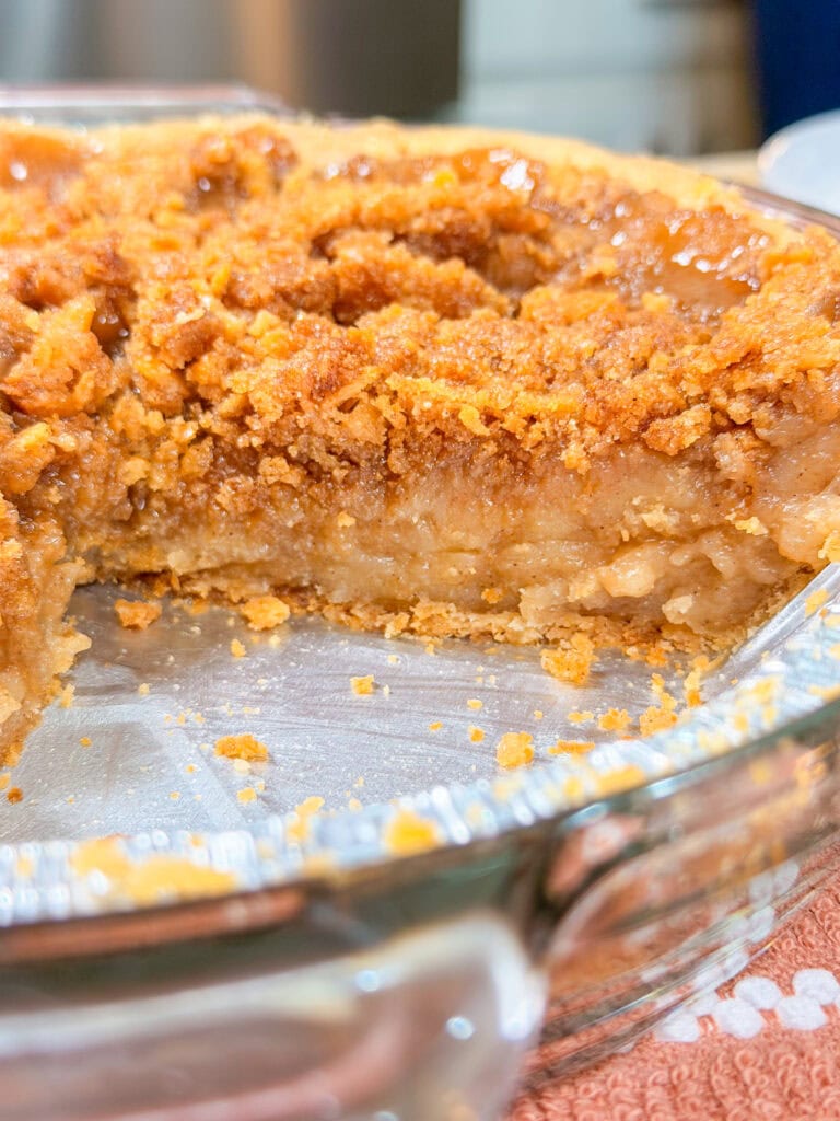 Close-up of a partially eaten pie in a glass dish, featuring a golden, crumbly topping and a gooey, caramelized filling.