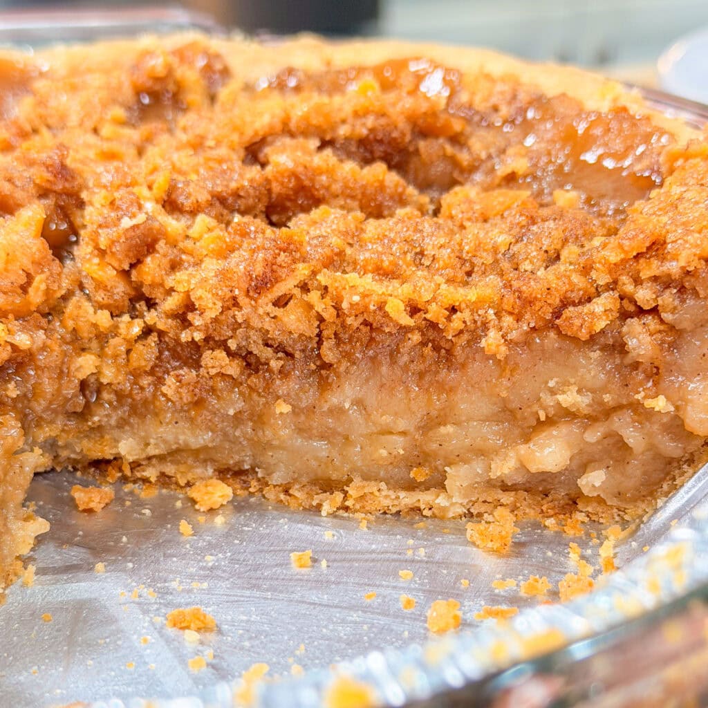 A close-up of a partially eaten pie with a thick, gooey filling and a crumbly, golden-brown topping in a metal pie tin.