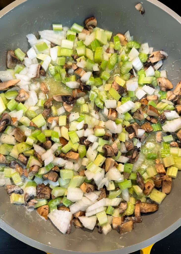 Chopped onions, celery, and mushrooms sautéing in a skillet.