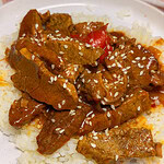 A plate of white rice topped with saucy beef strips, red bell peppers, and sprinkled with white sesame seeds.