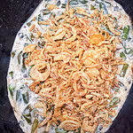 Green bean casserole topped with crispy fried onions, showing creamy green beans mixed with sauce and a generous layer of golden onions on top.
