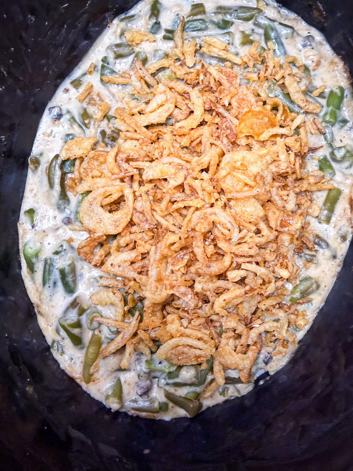 Green bean casserole topped with crispy fried onions, showing creamy green beans mixed with sauce and a generous layer of golden onions on top.