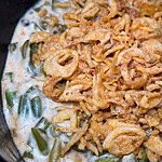 Green bean casserole topped with crispy fried onions in a creamy sauce, shown close up in a serving dish.