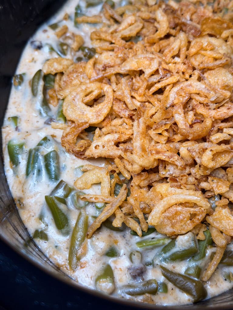 Green bean casserole topped with crispy fried onions in a creamy sauce, shown close up in a serving dish.