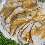 Sliced roast turkey breast topped with brown gravy on a white plate, garnished with fresh parsley.