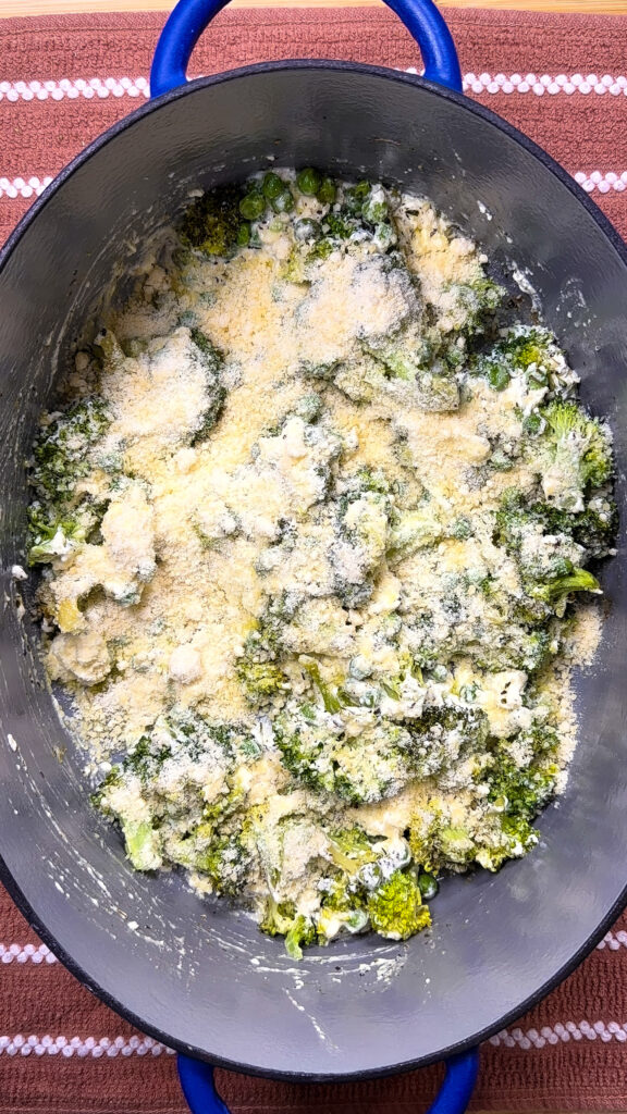 Broccoli florets in a large black pot, sprinkled with grated cheese or breadcrumbs, sit on a brown striped kitchen towel.