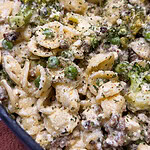 Close-up of orecchiette pasta mixed with ground meat, broccoli florets, green peas, and a creamy white sauce, garnished with herbs.