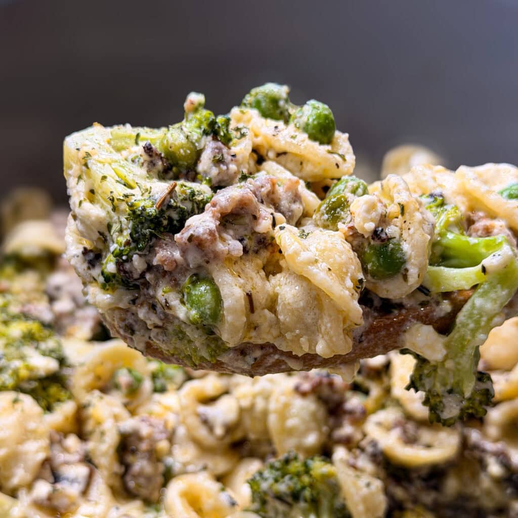 A close-up of a cheesy pasta dish with orecchiette, ground beef, broccoli, and peas, all coated in a creamy sauce.