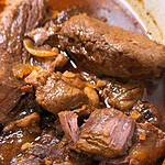 Close-up of tender, shredded pot roast beef in a rich brown sauce with visible onions in a white dish.