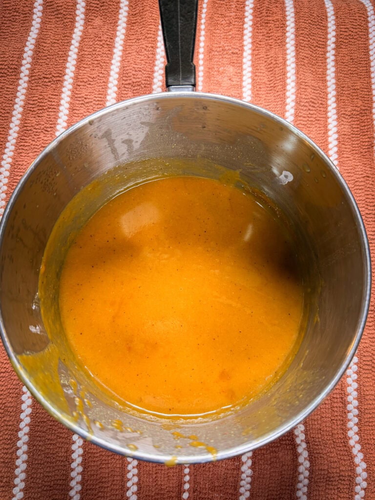 A saucepan filled with smooth orange sauce sits on a red and white striped towel.