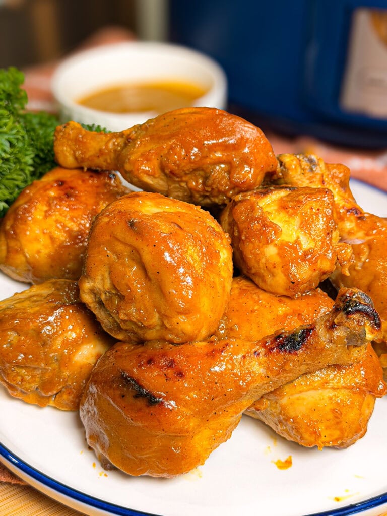 Plate of glazed, golden-brown chicken drumsticks and thighs, garnished with parsley, with a small bowl of sauce in the background.