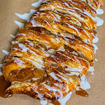 A braided pastry filled with cinnamon and apples, drizzled with white icing and caramel sauce, sits on brown parchment paper.