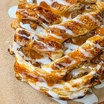 Close-up of a golden, braided pastry topped with white icing and caramel drizzle, showing a crisp texture and gooey filling, resting on parchment paper.