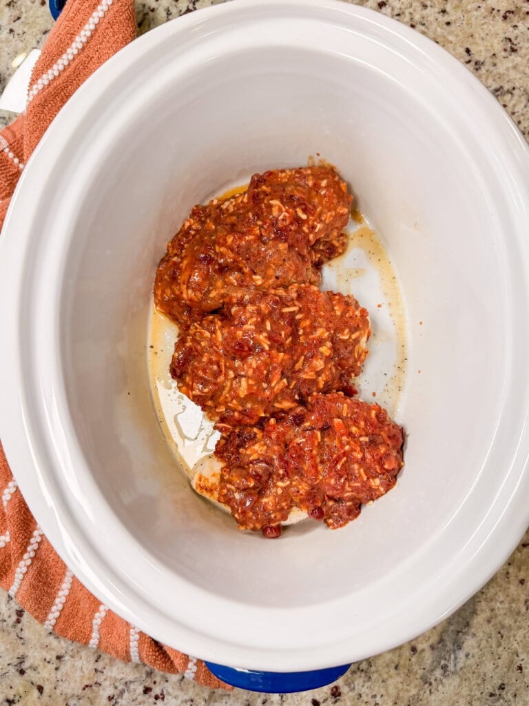 Three chicken breasts covered in red sauce inside a white slow cooker.