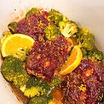 Meatballs topped with cranberry sauce and orange zest, served with broccoli florets and orange slices in a pot.