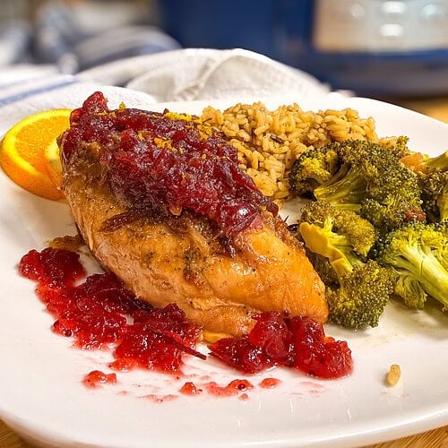 A chicken breast topped with cranberry sauce, served with rice and broccoli on a white plate.