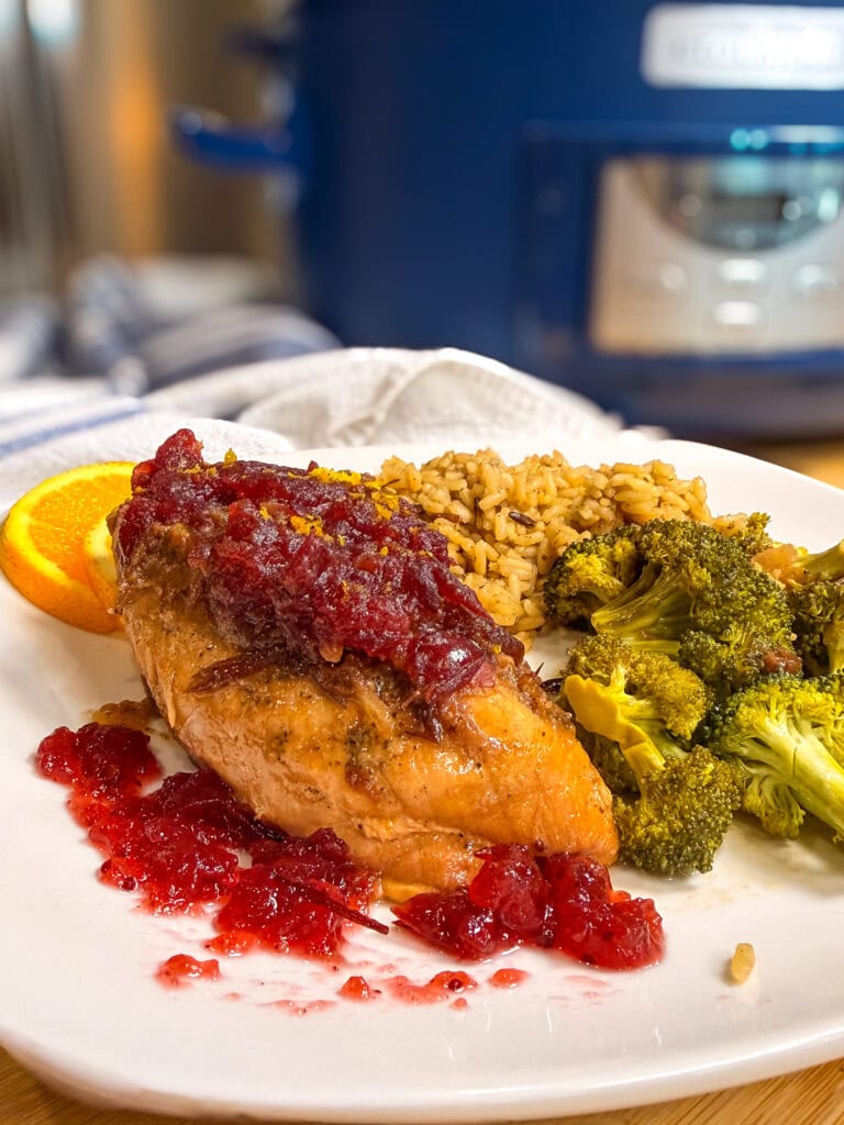 A chicken breast topped with cranberry sauce, served with rice and broccoli on a white plate.