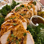 Sliced roasted turkey breast topped with brown gravy and garnished with parsley, served with extra sauce in a small cup and green herbs on a white plate.