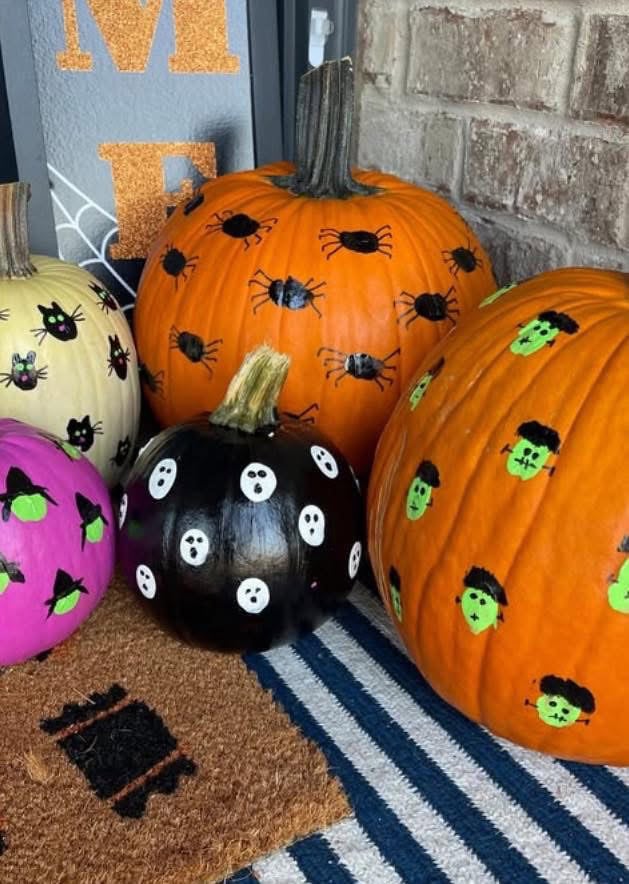Five pumpkins painted with Halloween designs, including spiders, ghosts, witch hats, and Frankenstein faces.