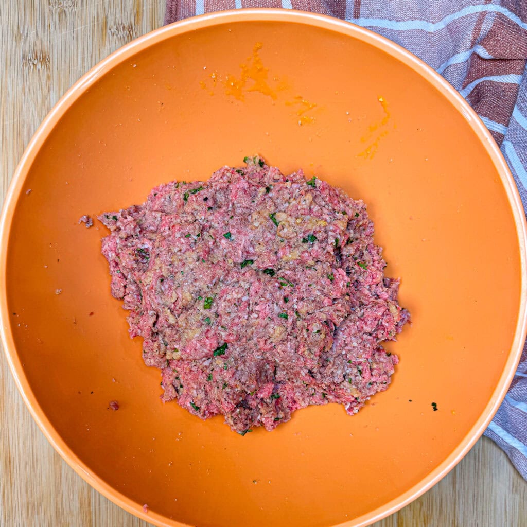 Raw seasoned ground meat in an orange mixing bowl.