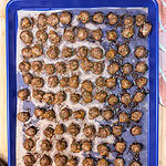 A large blue baking sheet lined with parchment paper covered in many small, freshly baked meatballs.