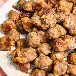 A pile of small, browned meatballs with visible flecks of herbs on a patterned plate.