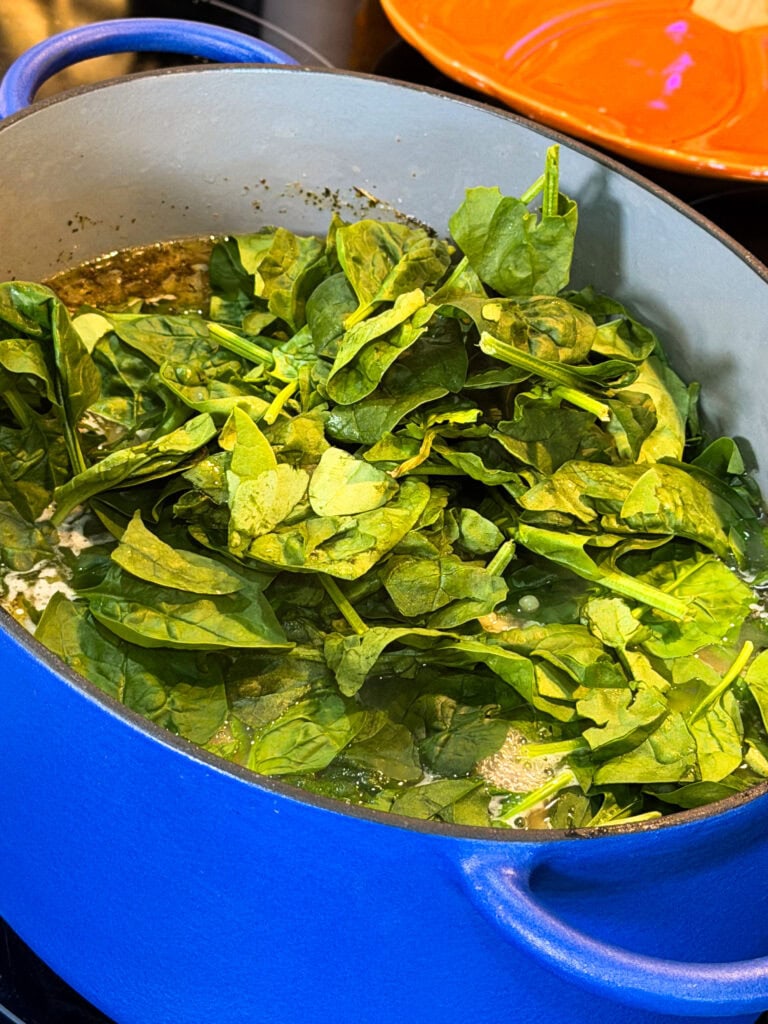 Fresh spinach wilting in a blue enameled Dutch oven.