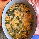 A blue Dutch oven filled with Italian wedding soup containing meatballs, spinach, and acini de pepe pasta.