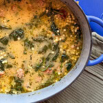 A Dutch oven filled with Italian wedding soup, featuring meatballs, tiny pasta pearls, and greens in a savory broth.