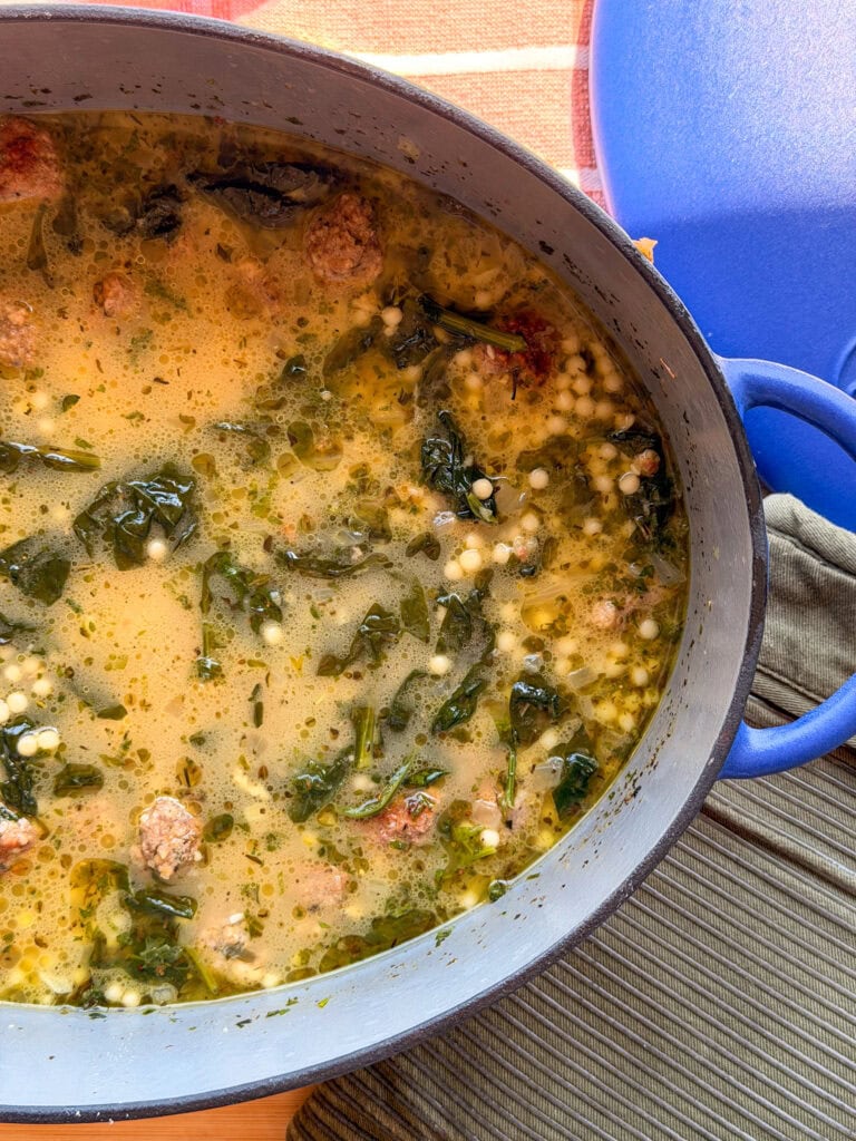 A Dutch oven filled with Italian wedding soup, featuring meatballs, tiny pasta pearls, and greens in a savory broth.