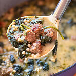 A ladle lifting wedding soup containing meatballs, leafy greens, and tiny pasta beads from a pot.