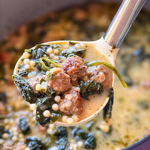 A ladle lifting wedding soup containing meatballs, leafy greens, and tiny pasta beads from a pot.