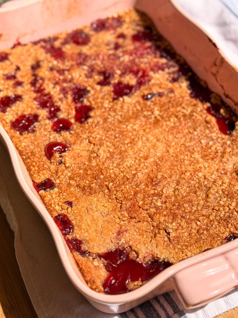 A pink ceramic baking dish filled with a baked fruit crisp topped with an oat crumble.