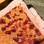 A fruit crumble with a golden-brown oat topping and patches of red berry filling in a rectangular pink baking dish.