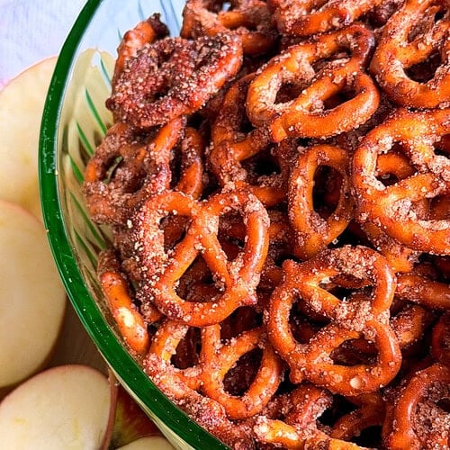A glass bowl filled with cinnamon-sugar coated pretzels, sitting next to sliced apples.