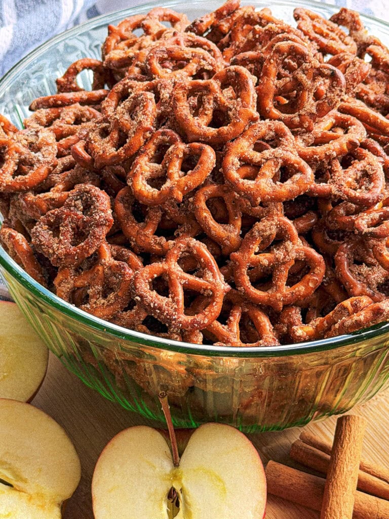 A large glass bowl filled with cinnamon sugar pretzels, surrounded by apple slices and cinnamon sticks.