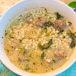 A bowl of Italian wedding soup containing tiny pasta pearls, meatballs, and greens.