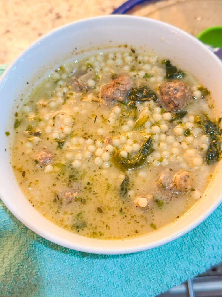 A bowl of Italian wedding soup containing tiny pasta pearls, meatballs, and greens.